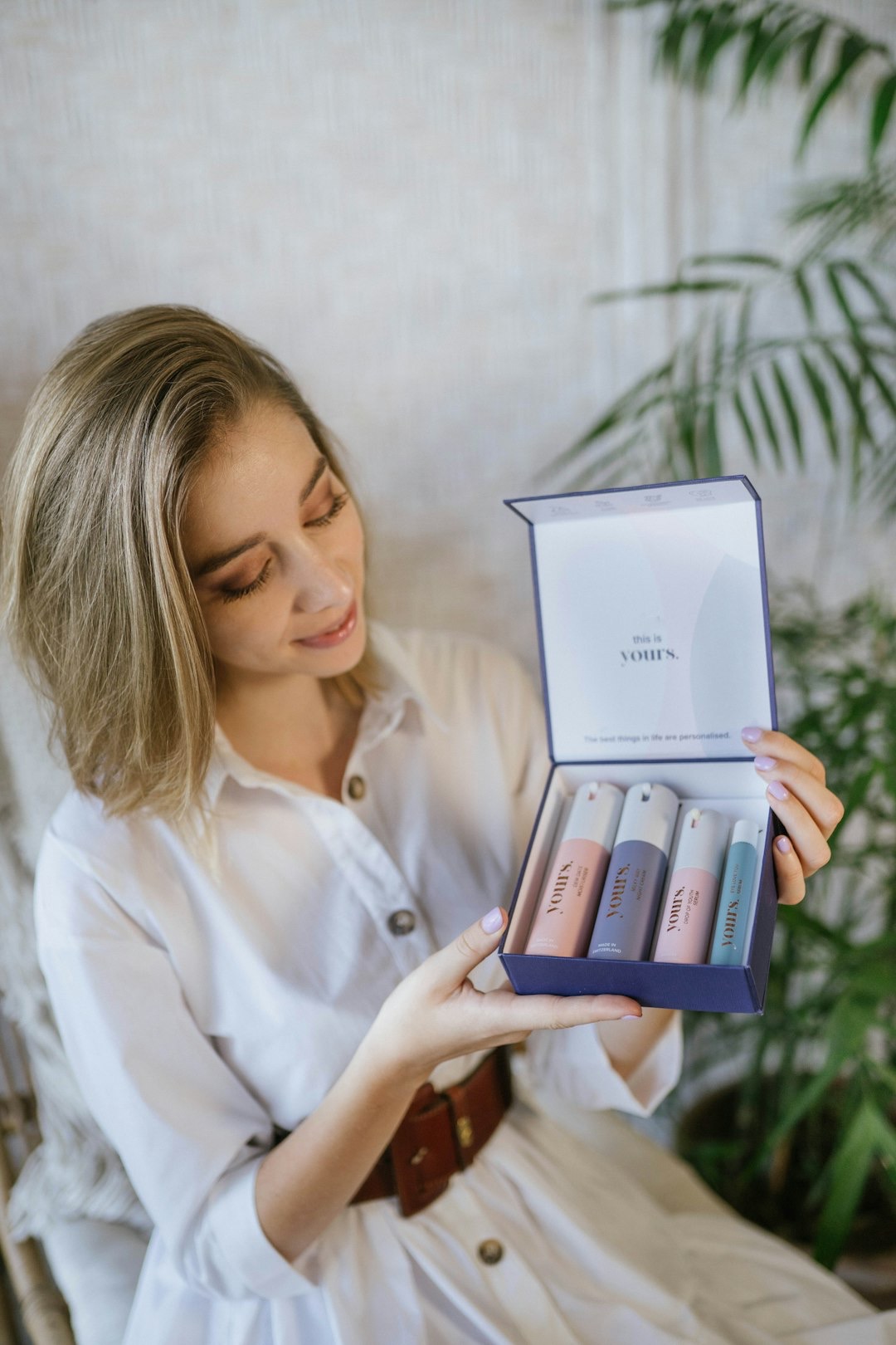 Woman smiles holding a navy blue box with skincare products.